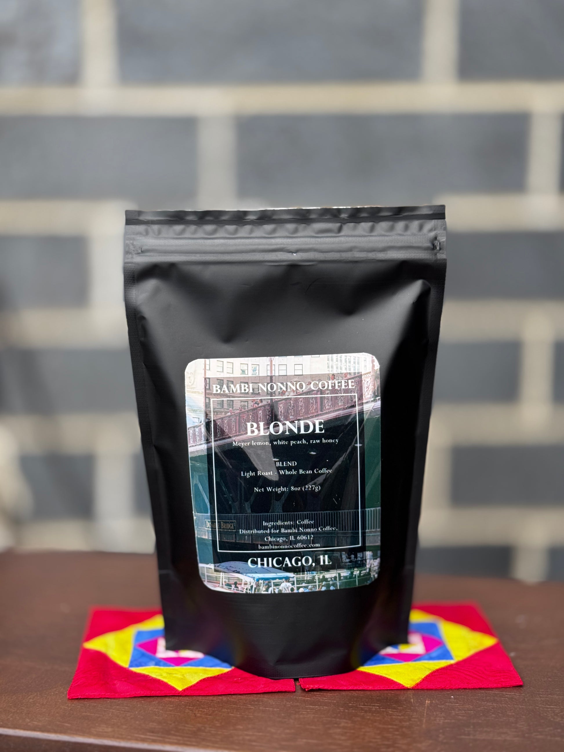 Black coffee bag labeled 'Blonde' on a colorful napkin with a gray tiled background