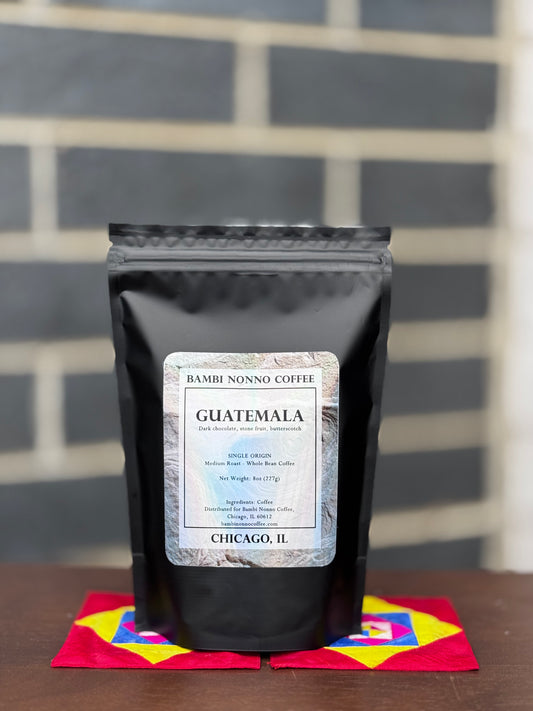 Black coffee bag with Guatemala label on a colorful napkin against a brick wall.